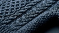 Dark gray knitted fabric with intricate cable pattern texture, close-up detail of wool sweater material for fashion and textile design projects.