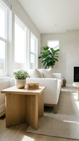Bright minimalist living room with white sofa, wooden side table, green plants, and natural light streaming through large windows.
