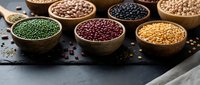 Assorted colorful legumes and beans in wooden bowls on dark slate surface. Healthy protein-rich ingredients for cooking and nutrition concepts.