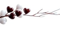 Red glass heart-shaped beads and white spherical beads arranged on delicate branch against white background, creating minimalist romantic composition.