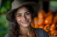 Young Hispanic woman with natural smile wearing brown hat at farmers market, fresh oranges in background. Candid portrait with warm lighting and soft bokeh effect.