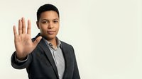 Young African American businessman in suit making stop gesture with hand raised, professional portrait on neutral background for business concepts.
