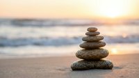 Zen stone stack balanced on sandy beach at golden sunset with soft ocean waves creating peaceful meditation and mindfulness atmosphere for wellness concepts.