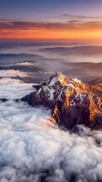 Majestic snow-capped mountain peak emerging through dramatic clouds at golden hour sunrise with vibrant orange and purple sky creating breathtaking alpine scenery.