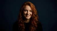 Portrait of smiling young Caucasian woman with curly red hair against dark background for professional headshot and business photography.