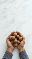 Overhead view of male hands holding walnuts in shells against white marble surface. Suitable for food, nutrition, healthy eating, and wellness content.