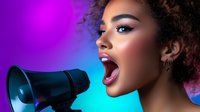 Young African American woman with curly hair speaking into megaphone with dramatic purple and blue lighting for activism and communication campaigns.