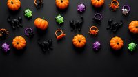 Halloween party decorations with orange pumpkins, black cats, colorful spiders and rings scattered on dark background for festive celebration design.