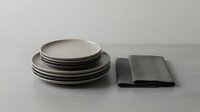 Stacked ceramic plates with dark rim and folded gray linen napkin on neutral surface for dining, tableware, and home decor styling.