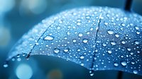 Raindrops on blue umbrella surface creating natural pattern with bokeh effect in background, macro photography showing water resistance and protection on rainy day.