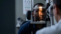 African American man receiving comprehensive eye examination from optometrist using advanced diagnostic equipment in modern medical clinic setting.