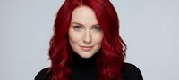 Professional redhead woman with vibrant red hair and blue eyes wearing black turtleneck sweater against neutral background for business portrait.