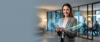 Young woman with long dark hair, Caucasian ethnicity, wearing a light gray blazer and white shirt, smiling while interacting with holographic digital interface displaying connected network icons and data visualization in modern office environment.