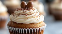 Vanilla cupcake topped with swirled buttercream frosting, chocolate eggs and sprinkles on blurred background. Sweet Easter dessert with creamy decoration.