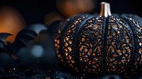 Black lace pumpkin with intricate carved pattern glowing with warm orange light against dark background, creating magical Halloween atmosphere.