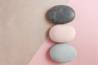Smooth spa stones stacked on pink and beige background. Minimalist zen composition with balanced pebbles creating calm, meditative atmosphere. Perfect for wellness designs.