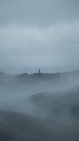 Solitary figure standing on misty mountain ridge at dawn, surrounded by layered fog and rolling hills, conveying isolation and contemplation for editorial and conceptual projects.