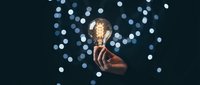 Hand holding glowing vintage Edison bulb against dark background with bokeh lights for creative inspiration and innovation concepts.