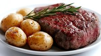 Juicy grilled beef steak cooked medium rare served with golden roasted baby potatoes and fresh rosemary sprig on white ceramic plate, close up food photography.