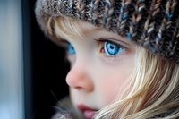 Close up portrait of young blonde girl with striking blue eyes wearing knitted winter hat, looking away in soft natural light. Artistic child photography.
