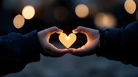 Silhouetted hands forming heart shape against glowing sunset with bokeh lights creating romantic atmosphere. Love gesture captures warm golden light.