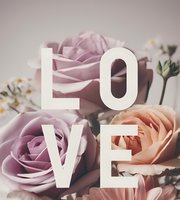 Romantic typography LOVE overlaid on soft pastel roses and delicate white flowers, creating an elegant wedding or Valentine's Day design.