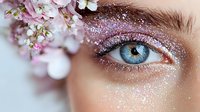 Close-up of blue eye with pink glitter makeup and cherry blossom flowers, artistic beauty portrait showcasing spring-inspired cosmetic application and floral elements.