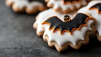 White and black bat shaped sugar cookies with orange icing details on dark background, Halloween festive homemade baked treats for holiday celebration.