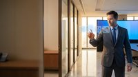 Professional businessman in suit walking through modern office corridor with glass walls and contemporary interior design for corporate presentations.