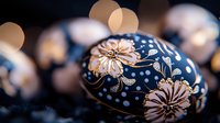 Decorative Easter egg with delicate floral pattern in dark blue and gold colors featuring hand-painted flowers and dots on blurred bokeh background.