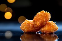Golden crispy chicken nuggets with crunchy coating on reflective surface against blurred bokeh lights background for food photography and menu design.