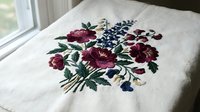 Embroidered floral bouquet with burgundy roses and blue flowers on natural linen fabric, traditional needlework craft for home decor and textile design.