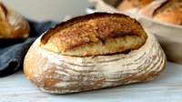 Freshly baked artisan sourdough bread with golden brown crust and flour dusting on rustic wooden surface, perfect for gourmet sandwiches.