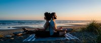 Young African American woman practicing meditation yoga on beach blanket during golden hour sunset with ocean waves and peaceful coastal scenery for wellness mindfulness.