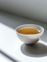White ceramic bowl with golden tea casting dramatic shadows on minimalist surface, natural light creating serene atmosphere for wellness and meditation concepts.