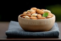Wooden bowl filled with mixed nuts including almonds and cashews on textured placemat, healthy snacking and natural nutrition concept for wellness lifestyle.
