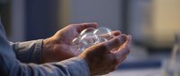 Male hands holding clear glass sphere with light reflection, symbolizing care, protection, and sustainable business solutions for corporate and environmental concepts.