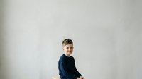 Young boy with light brown hair and fair complexion wearing dark navy blue sweater, smiling at camera against plain white background, suitable for family portraits, children's clothing catalogs, and educational materials.