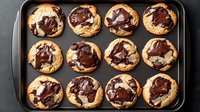 Fresh baked chocolate chip cookies with melted dark chocolate swirls on top arranged in baking tray, overhead view of homemade dessert treats.