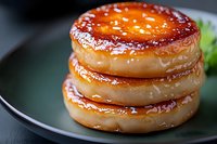 Stacked glazed donuts with caramelized sugar coating on dark plate. Close up view shows glistening amber surface and layered pastry texture. Fresh garnish adds color.