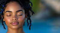 Young African American woman with natural locs hairstyle and glowing skin against blurred blue background, eyes closed in serene expression, showcasing natural beauty.