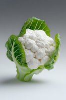Fresh cauliflower head with bright green leaves on light background, close up view showing detailed texture and natural pattern of vegetable florets.