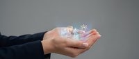 Professional businessman holding holographic digital icons in cupped hands representing modern technology, innovation and futuristic business concepts.