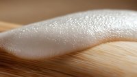 Macro shot of white foam or soap suds texture on wooden surface with soft focus and bokeh effect, creating abstract minimalist composition for spa and wellness designs.