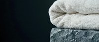 Folded beige towel stacked on textured gray stone surface against dark background, suitable for spa, wellness, and bathroom design projects.