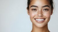 Young Asian woman with natural makeup and glowing skin smiling confidently against white background, showcasing fresh, healthy complexion and white teeth.