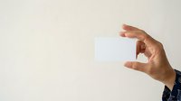 Cropped hand of male professional holding blank white card against neutral background for business branding and contact information display.