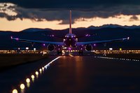 Commercial airplane on illuminated runway at dusk with dramatic sky and mountain silhouettes. Aviation transportation concept for travel industry.