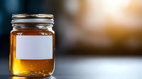 Glass mason jar filled with golden honey or maple syrup with blank white label on blurred warm background. Natural organic sweetener product photography.