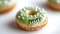 Green frosted monster donut with candy teeth and sugar pearl decorations on blurred background, creative Halloween party dessert for kids and celebrations.
